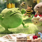 Toy frog wearing crown, cake-carrying bunny with bees celebrate birthday outdoors.
