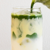 Green matcha tea being poured into a glass with milk and ice.