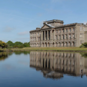 Large stately home reflected in water; nature and attractions on a sunny day.