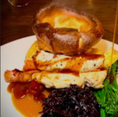 Roasted chicken with gravy, vegetables and Yorkshire pudding on a plate.
