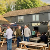 Patrons outside Nowhere bar in Bath, socializing around wooden tables and chairs.