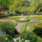 Formal garden with fountain surrounded by colorful flower beds and greenery.