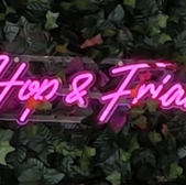 Neon sign that reads Hop & Friar against a backdrop of green leaves.