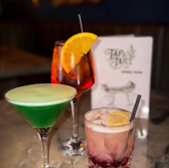 Three colorful cocktails, Tap & Tail menu on the table, perfect for a night out.