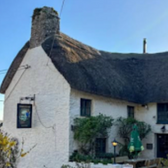 White building with thatched roof and sign, Newquay, against blue sky.
