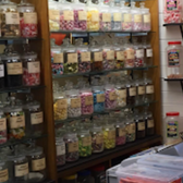 Shelves of assorted colorful candies in glass jars, various labels present.