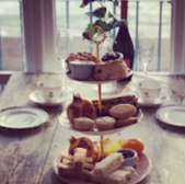 Afternoon tea with cakes, fruit, and wine on a rustic table setting.