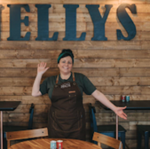 Woman waving, in Nellys Cafe with Nellys sign on wooden background