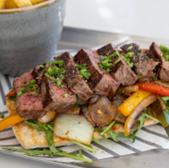 Steak sandwich with fries on a tray. Sliced steak with peppers and onions.