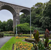 Stone viaduct over a pathway in a parkland setting with flowers and trees.