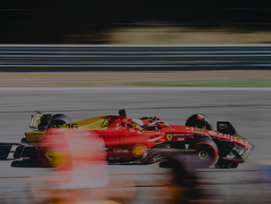 A red race car speeds on a track, with blurred surroundings indicating fast motion. Visible logos include Santander and Shell.
