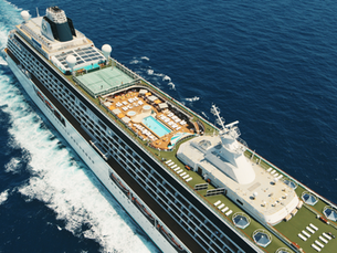 Aerial view of a white cruise ship slicing through deep blue sea, with pool deck and tennis court visible, wake trailing behind.