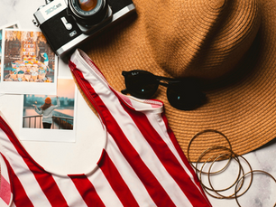 Camera, hat, sunglasses, red-striped swimsuit, and photos on marble surface. Vibrant travel mood with hints of adventure.