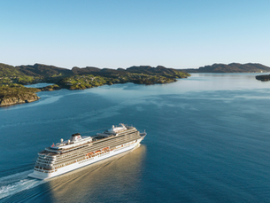 White Viking cruise ship sails across calm blue fjord past green islands under a clear sky.