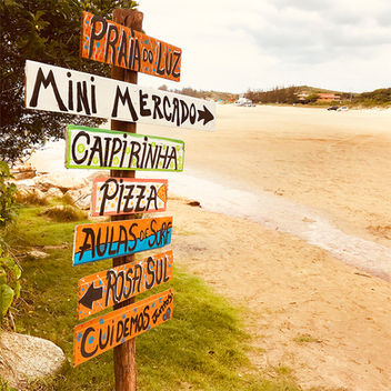 Placa da Praia do Luz com as indicações de mercados e comércios e a praia ao fundo.
