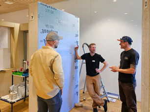 Three men chatting near a display of a SIGA wall membrane.