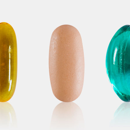 Five capsules aligned on a white background: orange, yellow, beige, teal, and green, each with reflective surfaces and smooth textures.