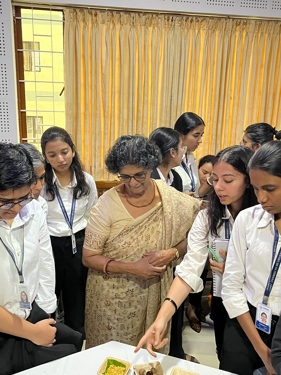 Group of students and woman viewing a table display, discussing it.