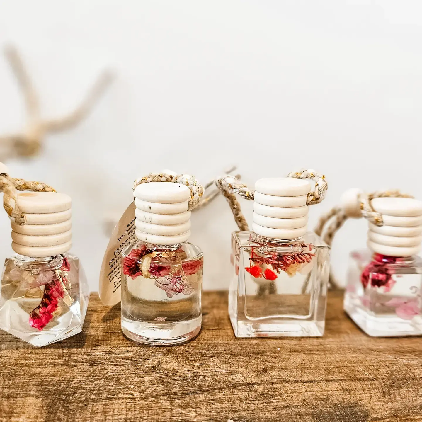 multiple shaped glass jars with flowers suspended in clear liquid. The cap is a beige ribbed texture with rope attached. 