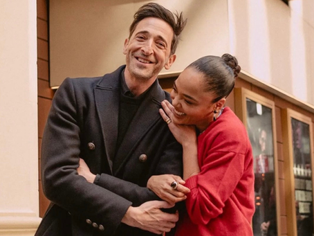 Two people smiling and walking together on a city street, sharing a warm, candid moment in stylish outfits.