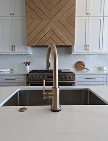 Center stage - custom white oak venthood in herringbone design above a 48" Monogram range. Surrounded by White Shaker style custom cabinetry with Chamoagne bronze pulls. This culinary haven features a deep single basin stainless steel sink with Delta Champagne Bronze touchless faucet and in counter push to start garbage disposal button in matching finish.