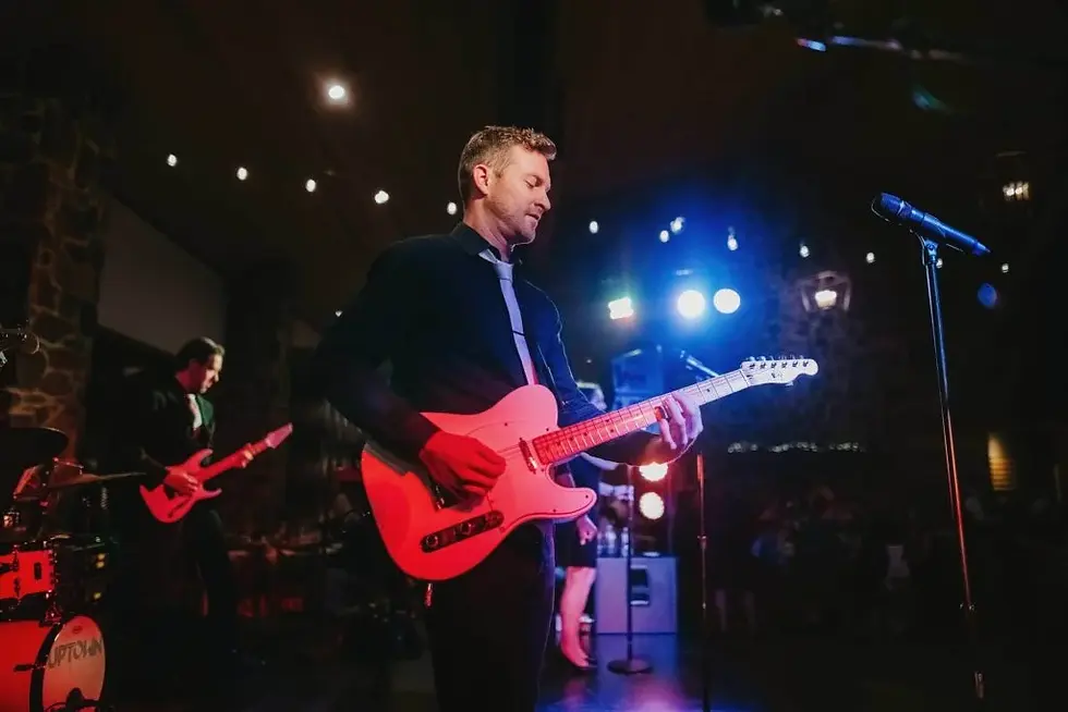 Live band karaoke performance with guitarists on illuminated stage with red and blue lighting