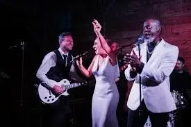 Live band performing on stage with guitarist, vocalist, and saxophonist under stage lighting at San Antonio bar