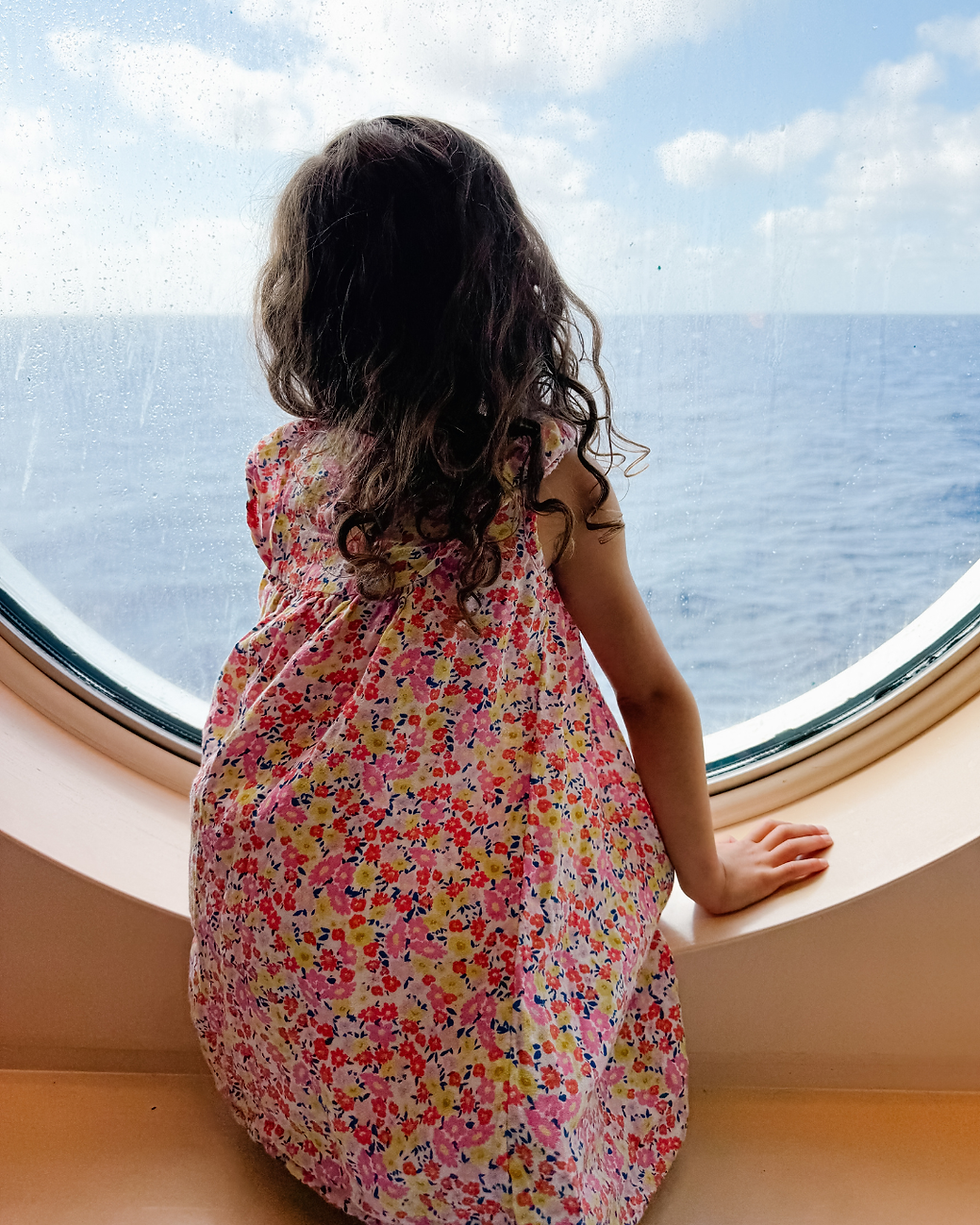 Young girl looking out a porthole on a cruise