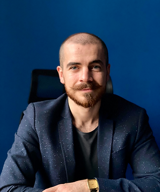 Управител облечен със син костюм, седнал на бюро позира на син форн