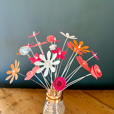 Small brightly coloured flowers made of card and displayed in a glass 'shaker'