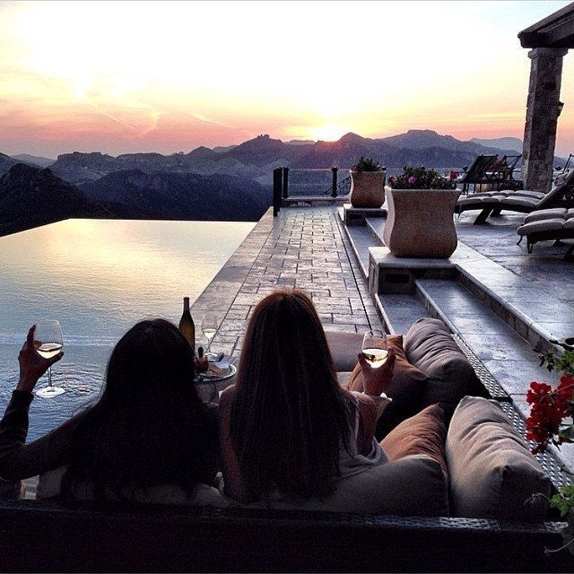 Две девушки с бокалами вина на веранде с видом на горы