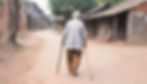 An old man walking on an empty village street with the help of a walking stick