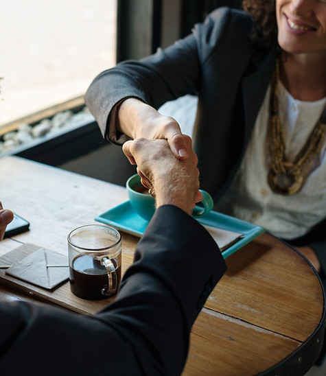 Woman smiling as she shakes hands with another man over coffee