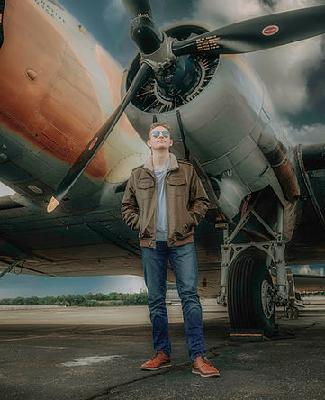A handsome high school senior poses with a WWII plane.