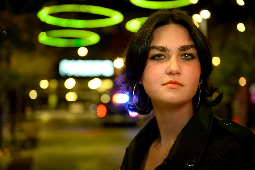Young woman with hoop earrings stands confidently at night, glowing green circles above. Blurred lights and text in background.