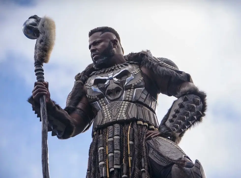 Armored warrior with fur-trimmed gear holds a staff against a cloudy sky, looking stern and powerful.