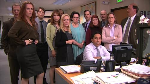 Worried office coworkers gather around a seated man at a cluttered desk under a green EXIT sign.