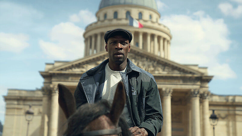 Man rides a horse in front of a grand domed building with a French flag under a blue sky.