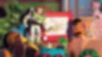 Toys gather around Buzz Lightyear pointing at a drawing on an Etch A Sketch. The scene is colorful and dynamic, set in a child's room.