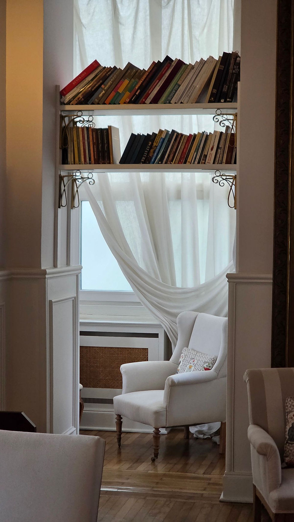 A classic armchair and bookshelf set beside a window.