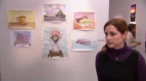 Woman stands in an art gallery beside pastel watercolor paintings on a wall, looking thoughtful and calm.