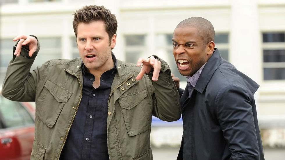 Two men making playful, claw-like gestures with expressive faces. They wear jackets, one olive and one navy. Background shows building windows.