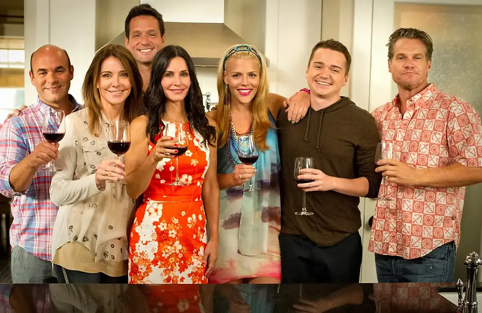 The Cougar Town cast poses together in a kitchen, several holding wine glasses.