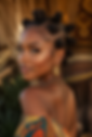 Portrait of a woman with braided buns, gold earrings, and a colorful off-shoulder dress against a warm, blurred background.