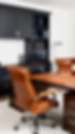 Modern office with tan leather chairs, dark wood desk, black built-ins, monitor, and lamp in a calm, tidy workspace