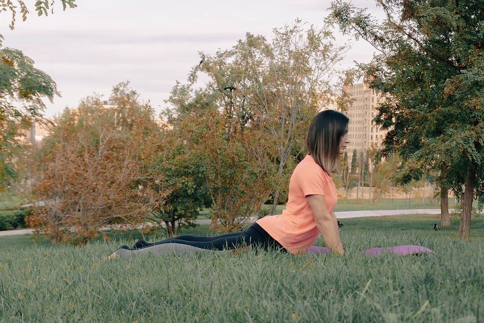A woman practises yoga on grass in a leafy urban park.