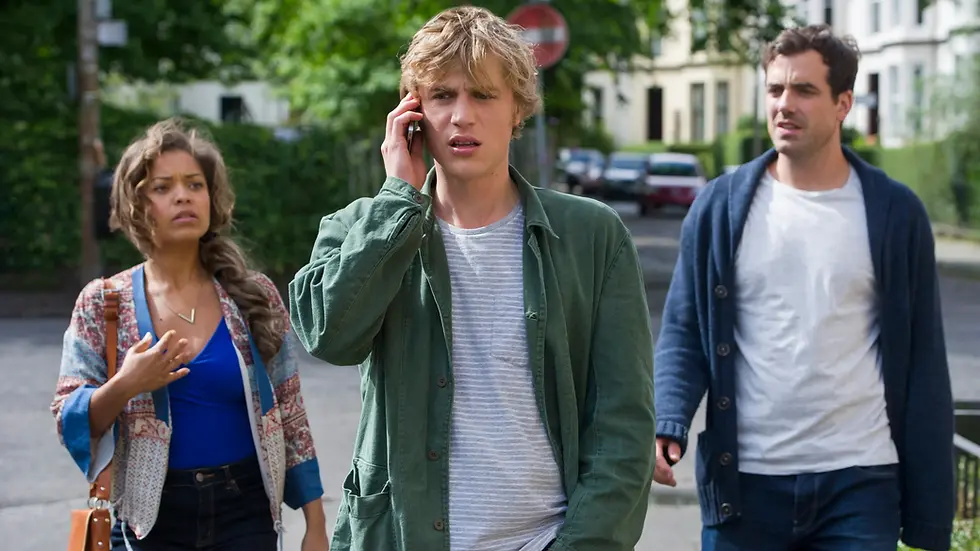 Three friends walk outdoors as the man in the center talks on a phone.