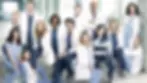 Group of doctors and nurses in white coats and blue scrubs posed in a bright hospital hallway, serious and confident.