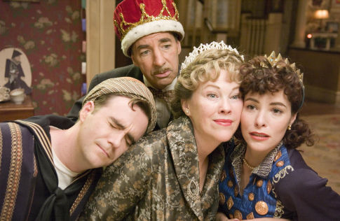 Four costumed adults huddle for a photo in a vintage parlor, one in a red crown, two women in ornate outfits, one man asleep.