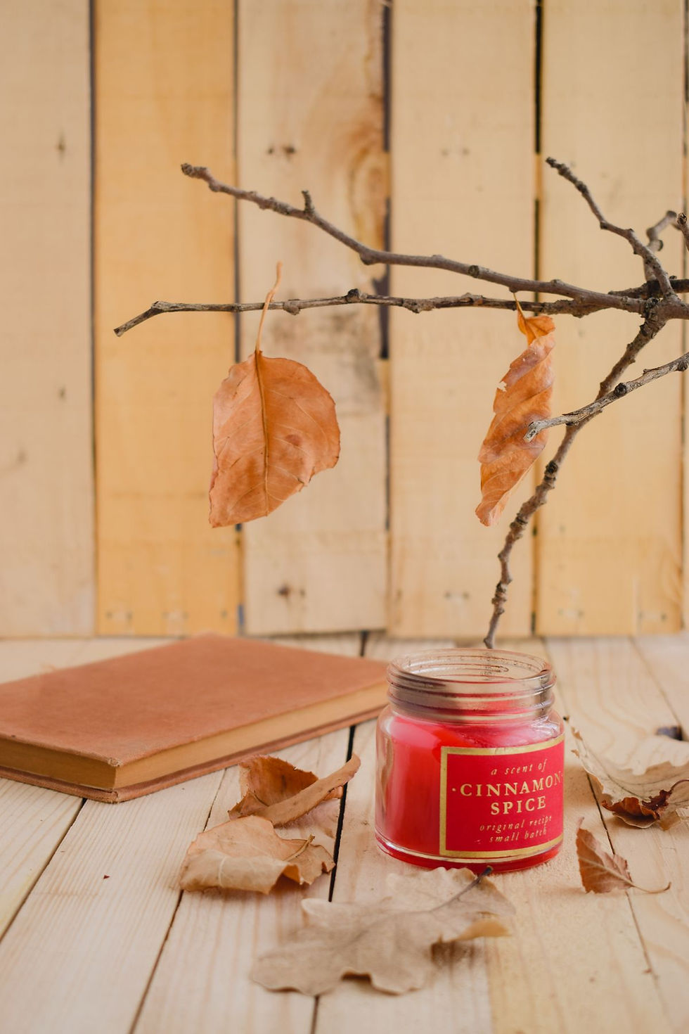 A cinnamon-scented candle with autumn leaves creating a warm seasonal atmosphere.